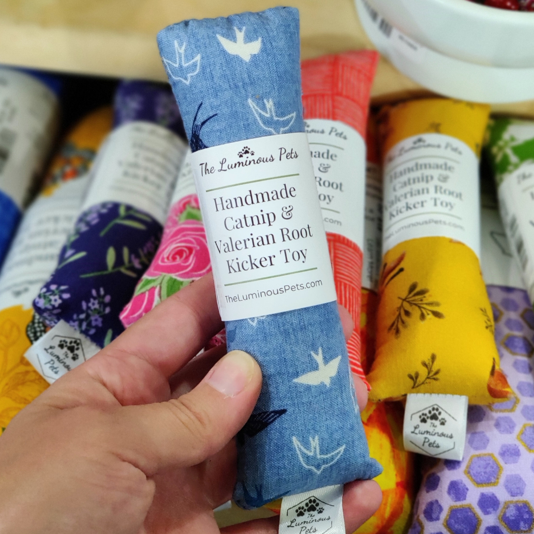 Handmade catnip and valerian root kicker toy with a blue pattern held by a hand, surrounded by other similar toys.